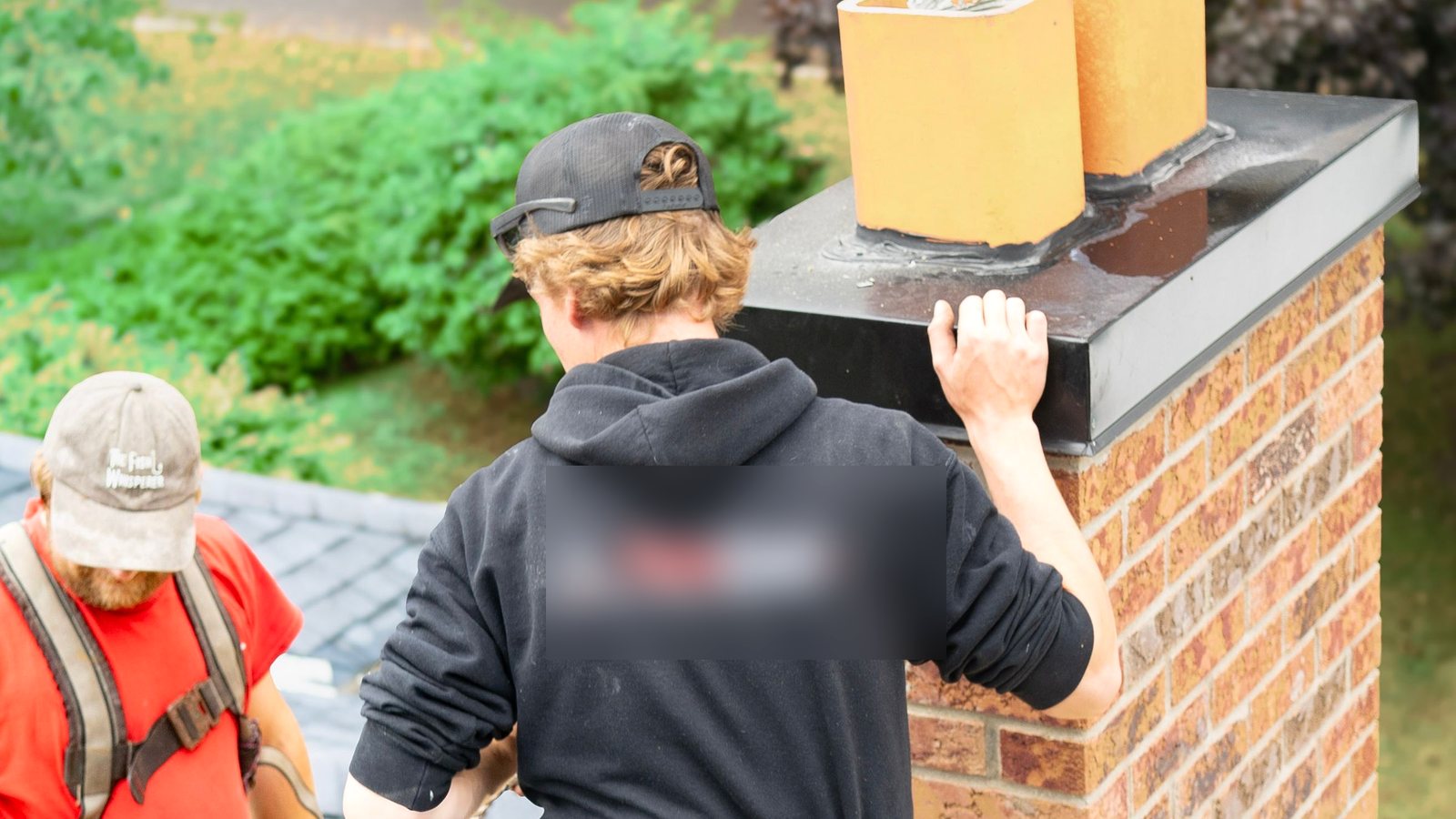 Workers inspecting a brick chimney on a roof.