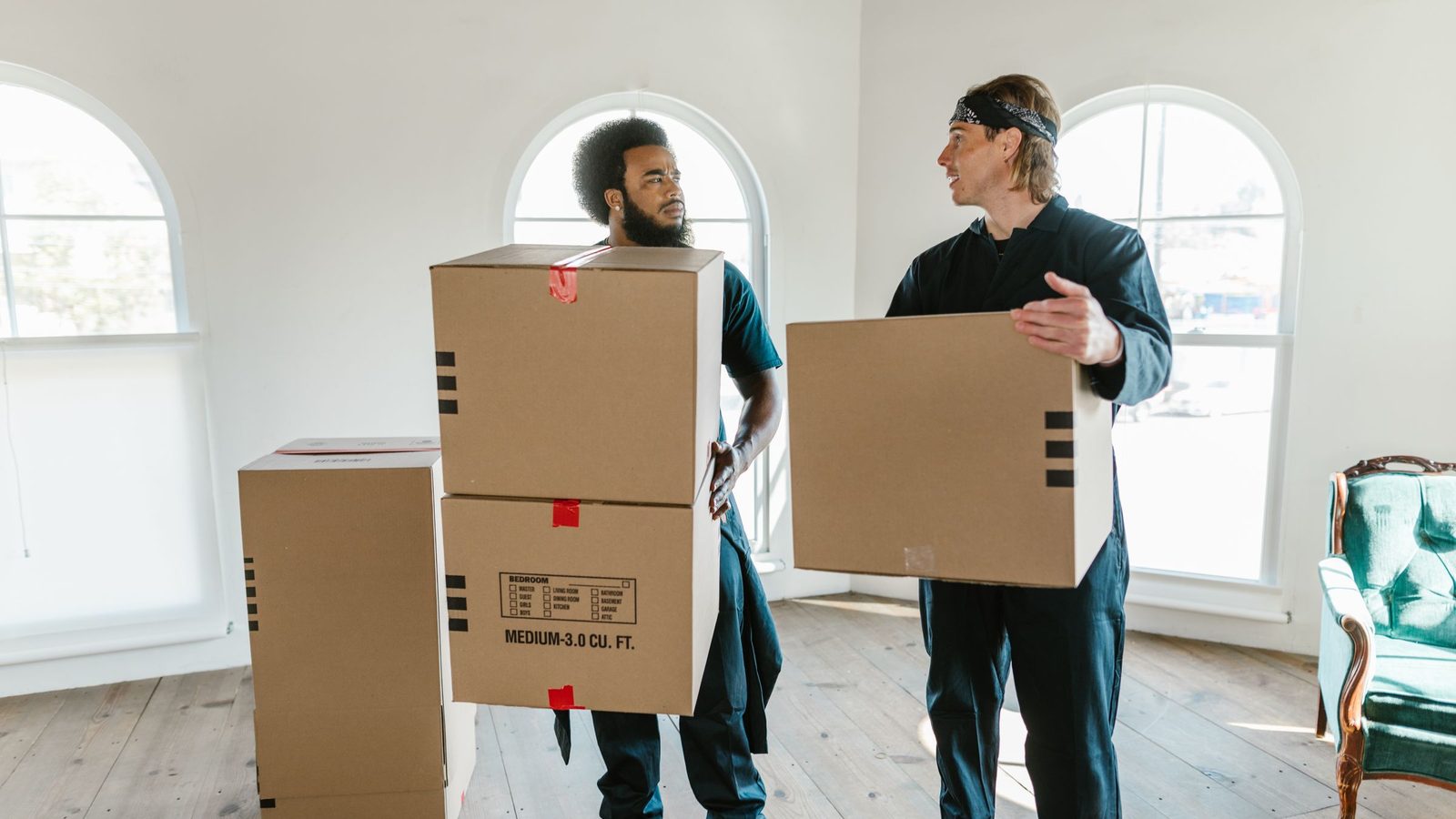 Two people carrying moving boxes inside a home.