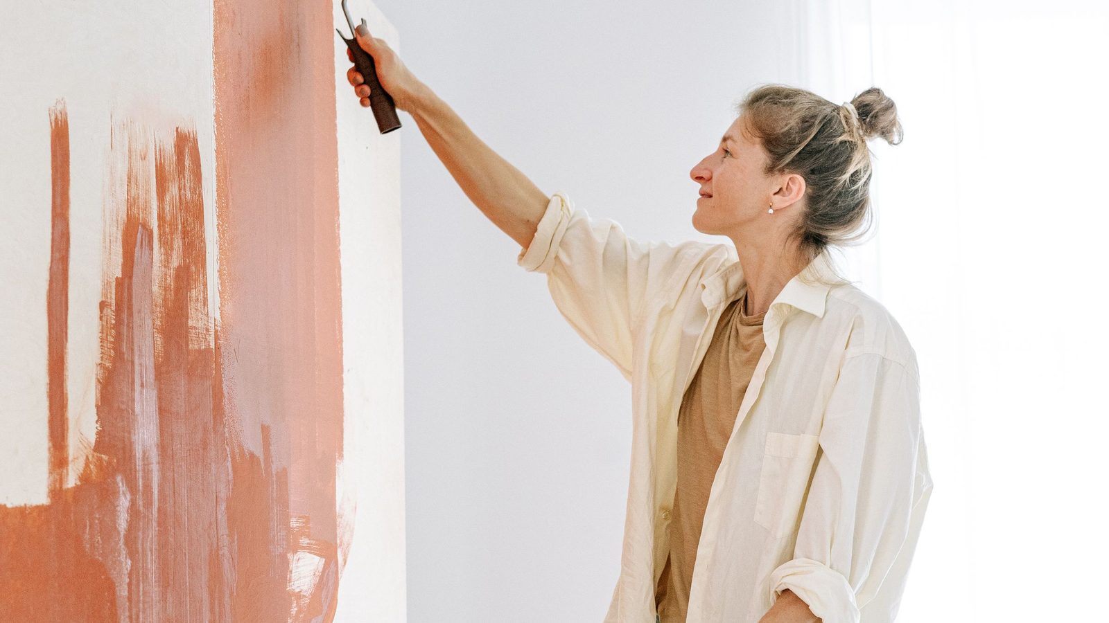 A person painting an interior wall from a stepladder.