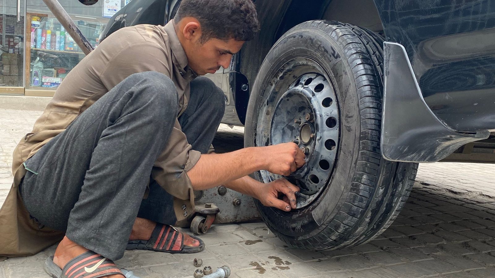 A person working on a vehicle wheel beside the road.
